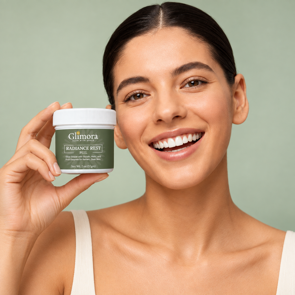 Model holding a GLIMORA RadianceRest Peel jar beside her face against a sage green background.