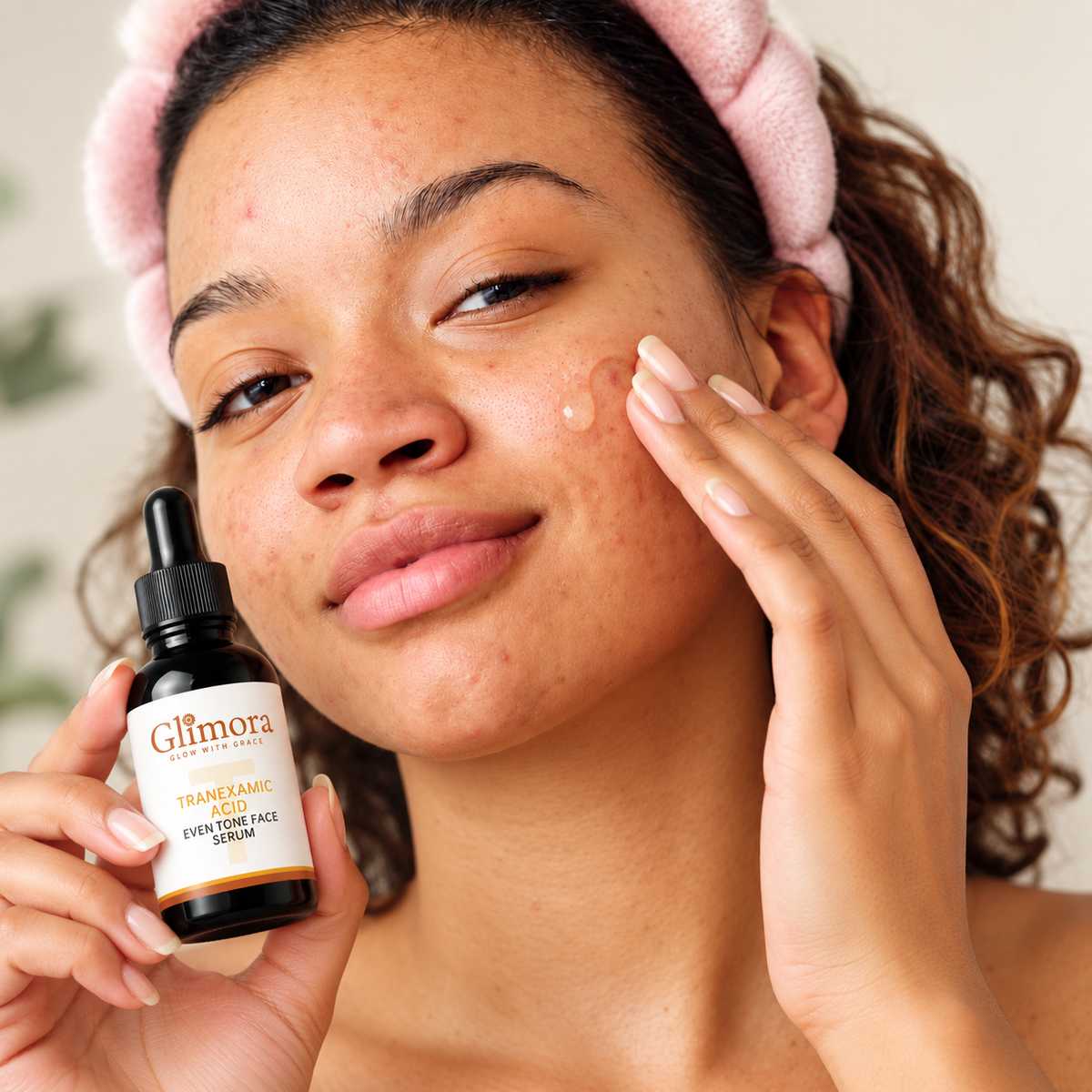 Model gently spreading GLIMORA Tranexamic Acid serum on her cheek while holding the bottle.